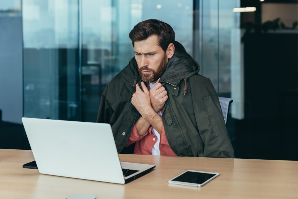 It's cold in the office, the businessman is freezing while working on a laptop inside the building